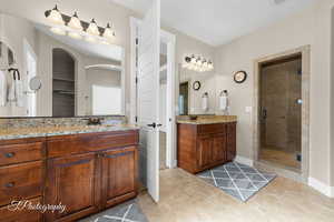 Bathroom featuring a shower stall, two vanities, and light tile patterned flooring