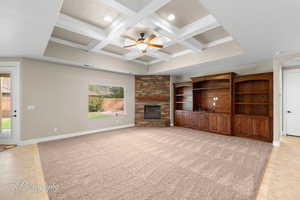 Unfurnished living room with beam ceiling, coffered ceiling, a ceiling fan, a stone fireplace, and light tile patterned floors