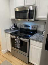 Kitchen with appliances with stainless steel finishes, white cabinets, light wood-style flooring, and dark stone countertops