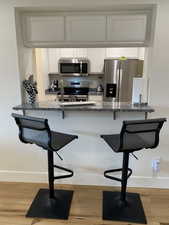 Kitchen featuring appliances with stainless steel finishes, a kitchen bar, white cabinetry, and a textured wall