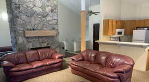 Carpeted living room featuring high vaulted ceiling, ceiling fan, and a fireplace