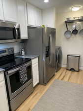 Kitchen featuring stainless steel appliances, white cabinetry, light wood-style floors, washer / dryer, and dark stone countertops