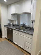 Kitchen featuring white cabinetry, light wood-style floors, dishwasher, dark stone counters, and recessed lighting