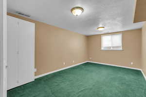 Carpeted spare room featuring a textured ceiling and baseboards
