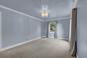 Carpeted empty room with ornamental molding and a chandelier