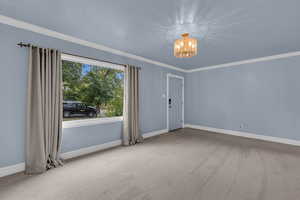 Carpeted empty room featuring crown molding and a chandelier