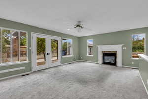 Unfurnished living room with french doors, carpet, a premium fireplace, and a ceiling fan