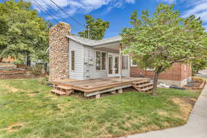 View of front of property with a wooden deck, a front lawn, french doors, a chimney, and brick siding