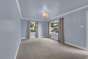 Carpeted spare room featuring crown molding and a chandelier
