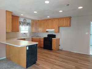 Kitchen featuring black gas range oven, a peninsula, light countertops, light wood finished floors, and recessed lighting