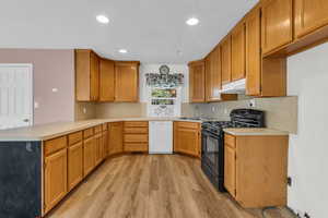 Kitchen featuring black gas range, a peninsula, light countertops, dishwashing machine, and light wood-type flooring