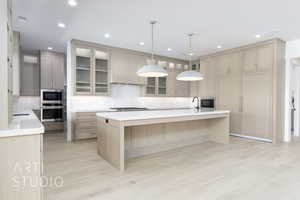 Kitchen featuring a center island with sink, a kitchen breakfast bar, light stone countertops, glass insert cabinets, and recessed lighting