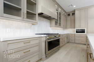 Kitchen featuring stainless steel stove, wall chimney exhaust hood, light wood finished floors, tasteful backsplash, and white microwave