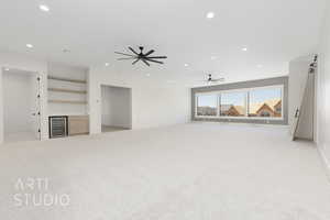Unfurnished living room with a barn door, light colored carpet, recessed lighting, and wine cooler