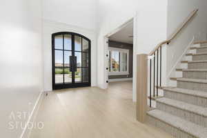 Foyer entrance with stairs, light wood-type flooring, a high ceiling, and french doors