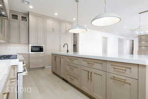 Kitchen featuring light stone counters, gas stove, decorative light fixtures, light brown cabinets, and recessed lighting