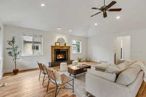 Living room with recessed lighting, light wood-style floors, lofted ceiling, a glass covered fireplace, and a ceiling fan