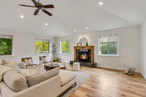 Living room featuring light wood-type flooring, recessed lighting, a fireplace, a ceiling fan, and vaulted ceiling