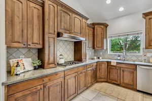 Kitchen with brown cabinetry, vaulted ceiling, appliances with stainless steel finishes, light tile patterned floors, and recessed lighting