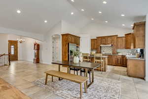 Kitchen featuring brown cabinetry, a center island, a breakfast bar area, tasteful backsplash, and high vaulted ceiling