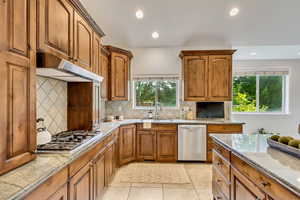 Kitchen featuring brown cabinetry, decorative backsplash, stainless steel appliances, recessed lighting, and healthy amount of natural light
