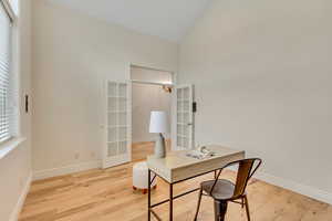 Home office featuring light wood finished floors, high vaulted ceiling, and french doors