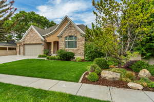 View of front of house with a front yard, driveway, brick siding, and an attached garage