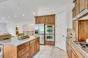 Kitchen featuring light stone countertops, appliances with stainless steel finishes, recessed lighting, brown cabinets, and light tile patterned flooring
