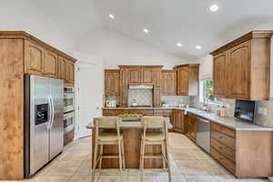 Kitchen with brown cabinets, stainless steel appliances, backsplash, a kitchen island, and light tile patterned flooring