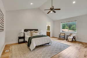 Bedroom with high vaulted ceiling, light wood-type flooring, a ceiling fan, connected bathroom, and recessed lighting