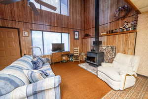 Living area with a towering ceiling, a wood stove, wood walls, carpet floors, and ceiling fan