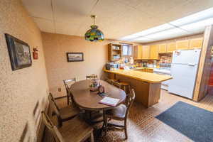 Kitchen with light countertops, white appliances, a peninsula, hanging light fixtures, and a paneled ceiling