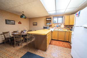 Kitchen featuring a peninsula, freestanding refrigerator, open shelves, light countertops, and a drop ceiling