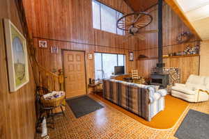 Living area featuring wooden walls, a wood stove, a high ceiling, and a ceiling fan