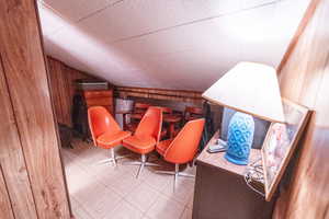 Living area featuring tile patterned floors, wooden walls, and lofted ceiling
