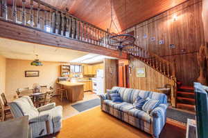 Living room with a high ceiling, stairway, light colored carpet, and wood walls