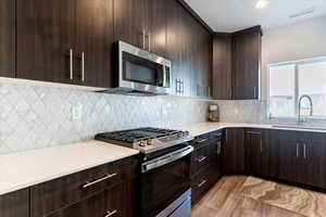 Kitchen featuring dark brown cabinets, appliances with stainless steel finishes, modern cabinets, light wood-style floors, and tasteful backsplash