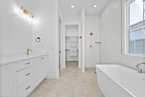 Full bath with a soaking tub, vanity, a walk in shower, a spacious closet, and recessed lighting