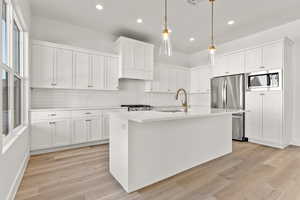 Kitchen featuring decorative backsplash, white cabinetry, stainless steel appliances, a center island with sink, and recessed lighting