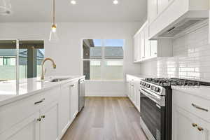 Kitchen with stainless steel appliances, white cabinets, custom range hood, light wood finished floors, and recessed lighting