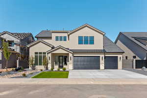 View of front facade featuring driveway, stucco siding, a standing seam roof, and a metal roof