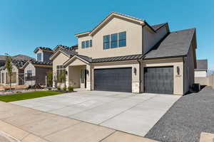 View of front facade with driveway, stucco siding, a standing seam roof, and stone siding