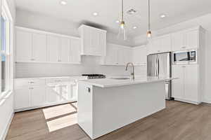 Kitchen featuring decorative backsplash, white cabinetry, appliances with stainless steel finishes, a center island with sink, and recessed lighting