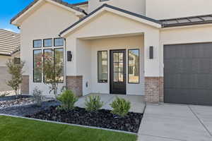 Entrance to property featuring stucco siding, brick siding, an attached garage, and concrete driveway