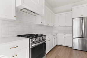 Kitchen featuring stainless steel appliances, custom exhaust hood, tasteful backsplash, white cabinetry, and light wood-style floors