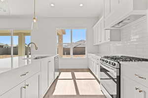 Kitchen featuring white cabinetry, appliances with stainless steel finishes, custom range hood, hanging light fixtures, and light wood-type flooring