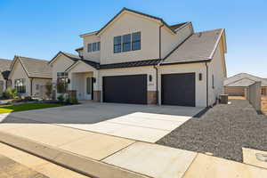 Modern farmhouse style home featuring driveway, stucco siding, brick siding, and a standing seam roof