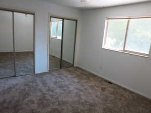 Unfurnished bedroom featuring two closets, multiple windows, and carpet flooring