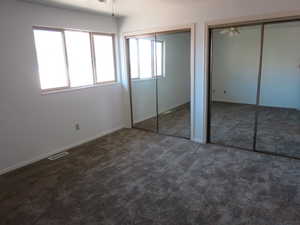 Unfurnished bedroom with two closets, dark colored carpet, and a ceiling fan
