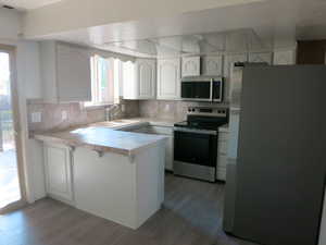 Kitchen with appliances with stainless steel finishes, white cabinets, a peninsula, and decorative backsplash